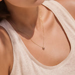 Close-up of a woman wearing a gold necklace with a small triangle red garnet pendant.