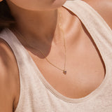 Close-up of a woman wearing a gold necklace with a small triangle red garnet pendant.
