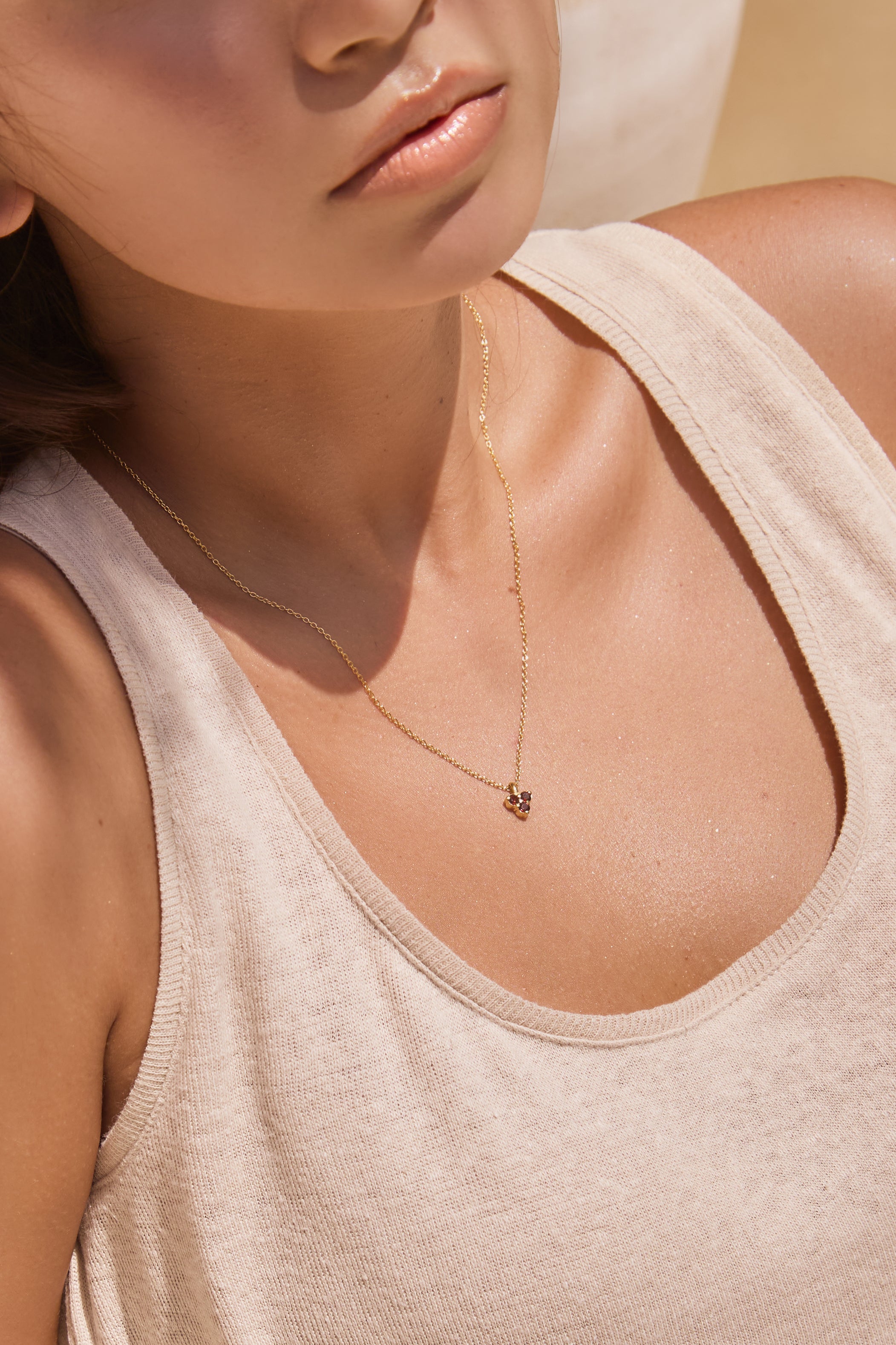 Close-up of a woman wearing a gold necklace with a small triangle red garnet pendant.