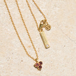 Gold necklace with triangle red garnet pendant and tag on a beige background