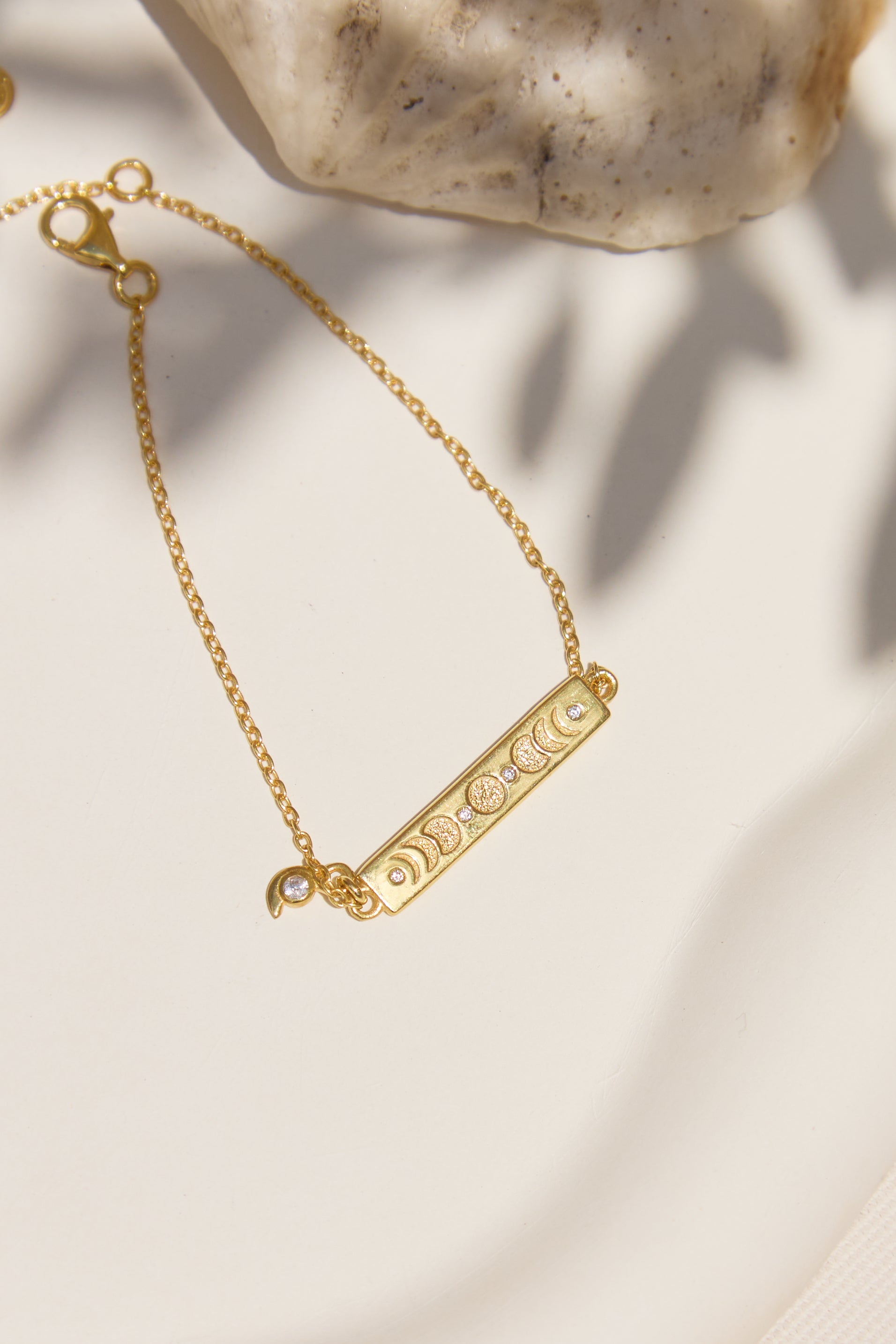 Gold bracelet with a bar design and moon phases on a neutral background