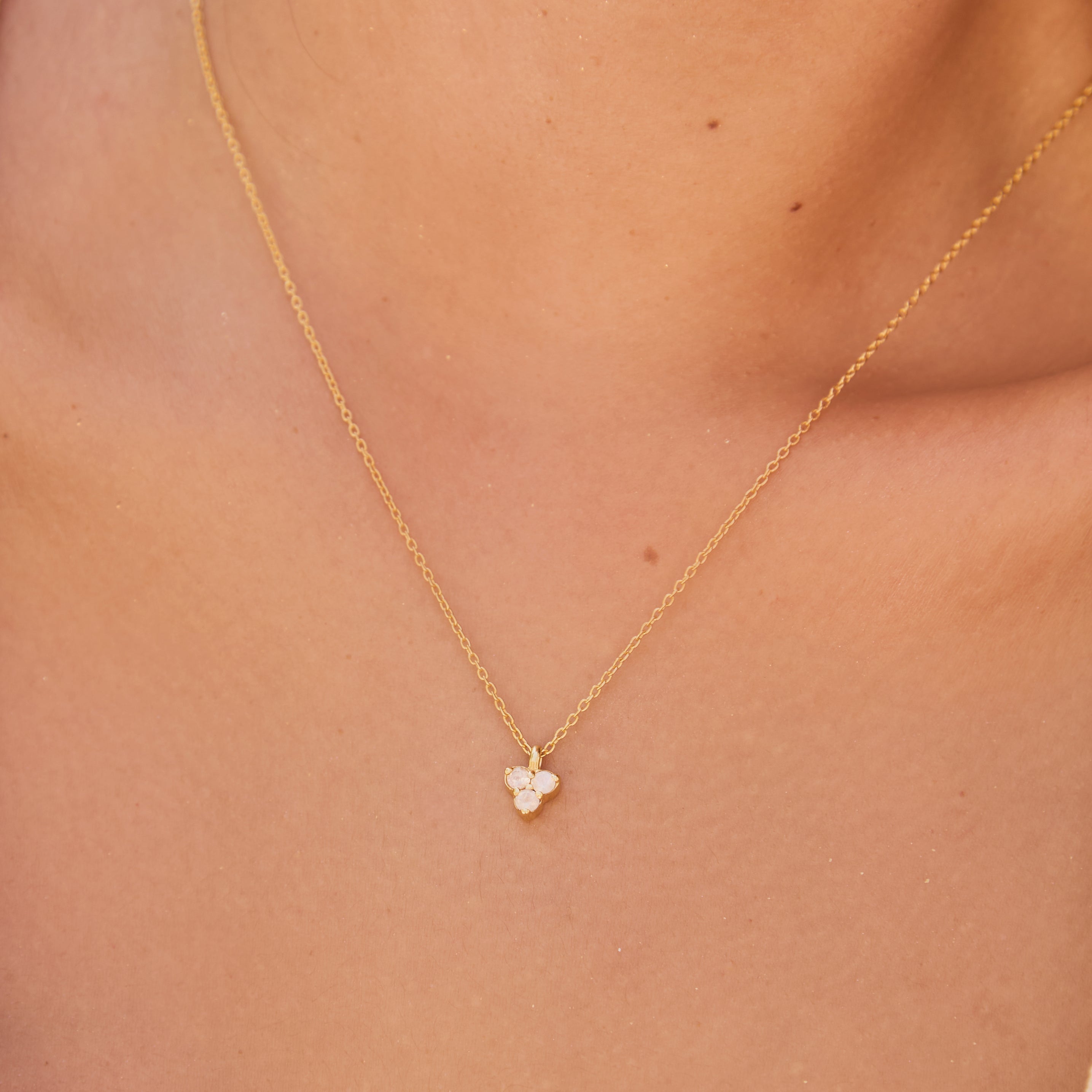 Gold necklace with a triangle-shaped moon stone pendant on a person's neck
