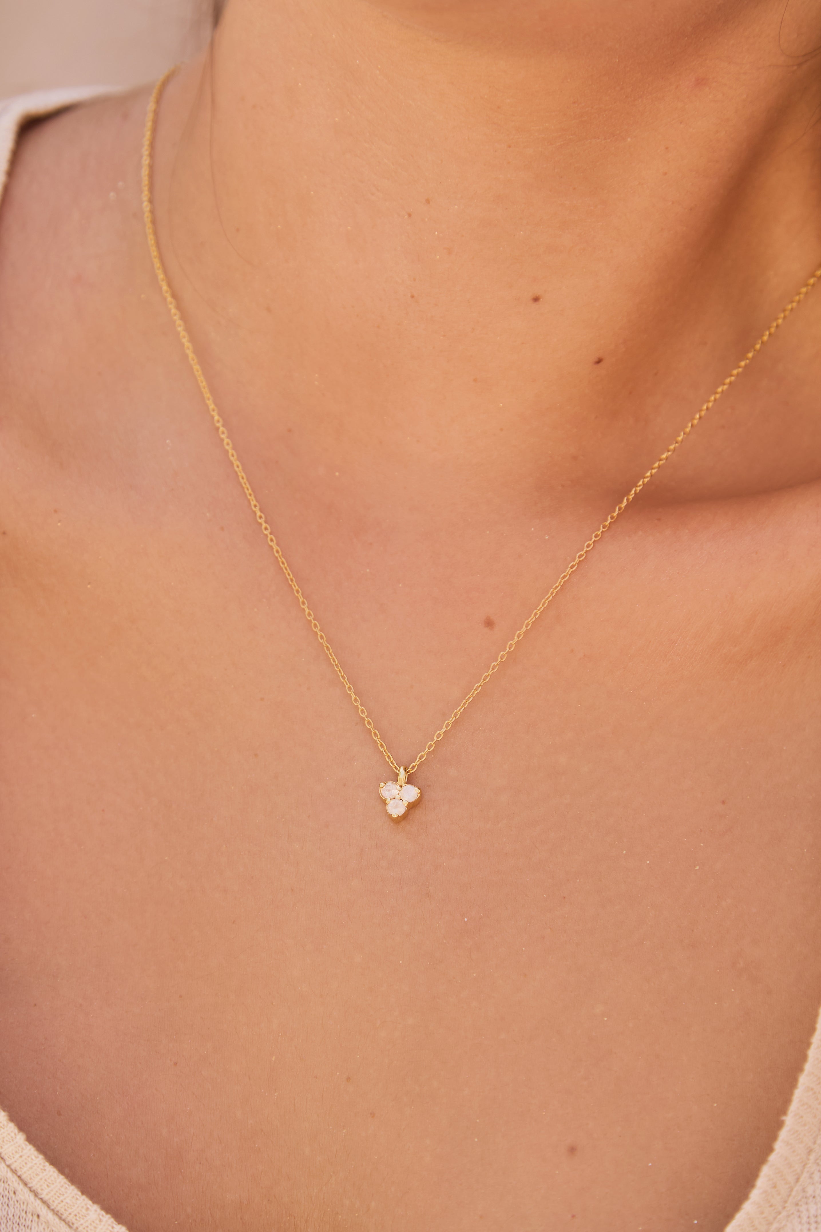 Gold necklace with a triangle-shaped moon stone pendant on a person's neck