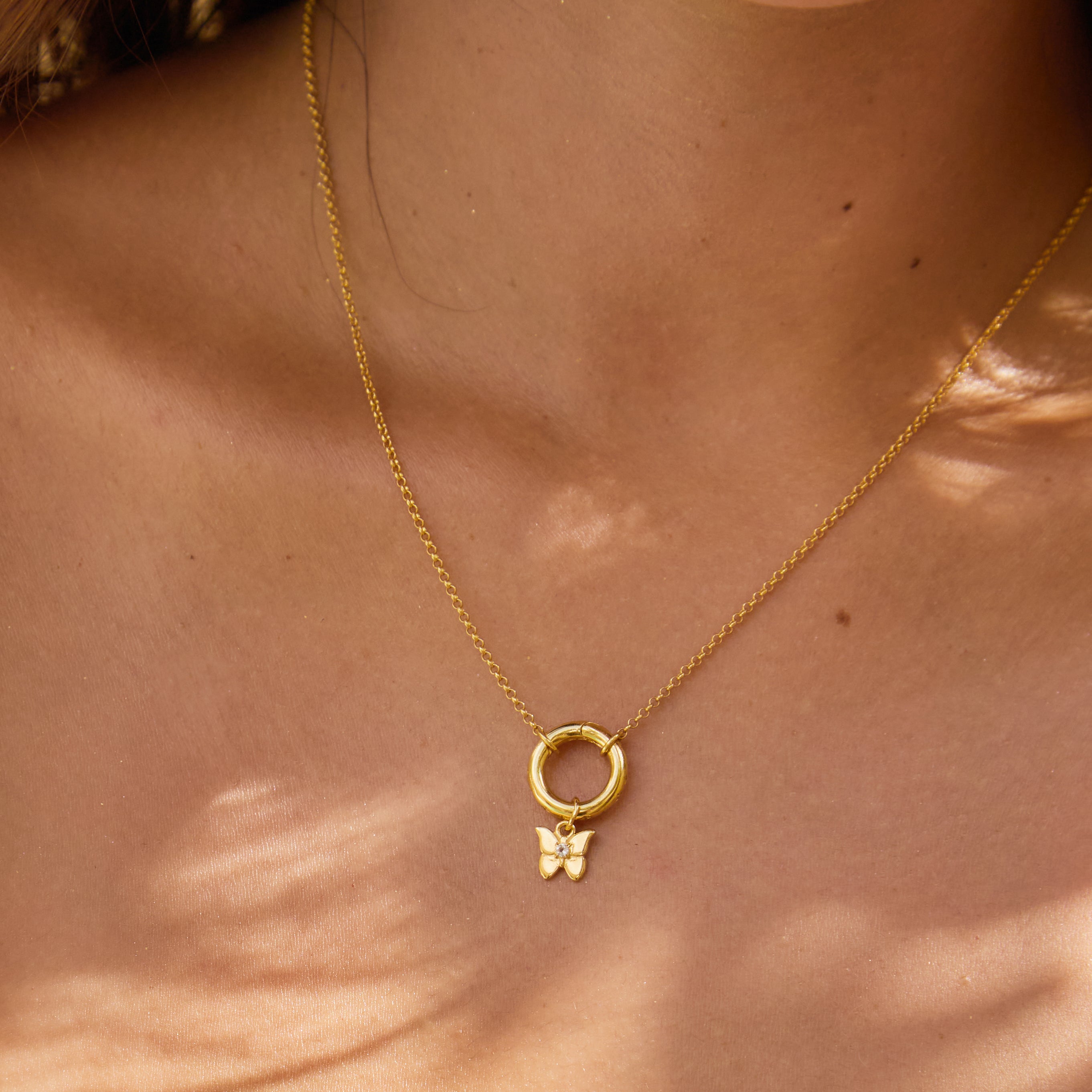 Close-up of a gold necklace with a small butterfly pendant on a person's neck.