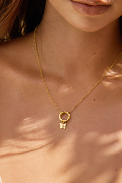Close-up of a gold necklace with a small butterfly pendant on a person's neck.