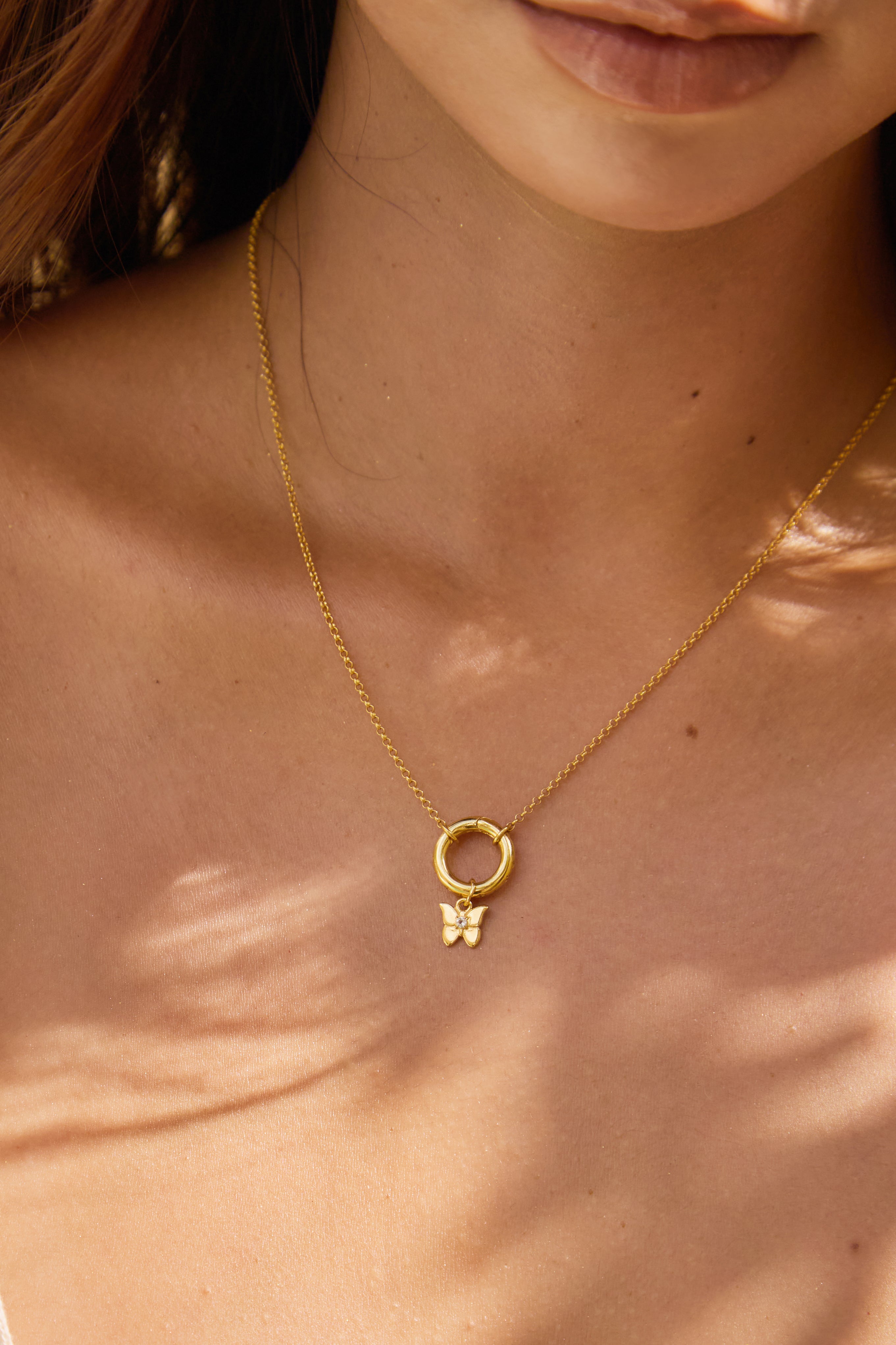 Close-up of a gold necklace with a small butterfly pendant on a person's neck.