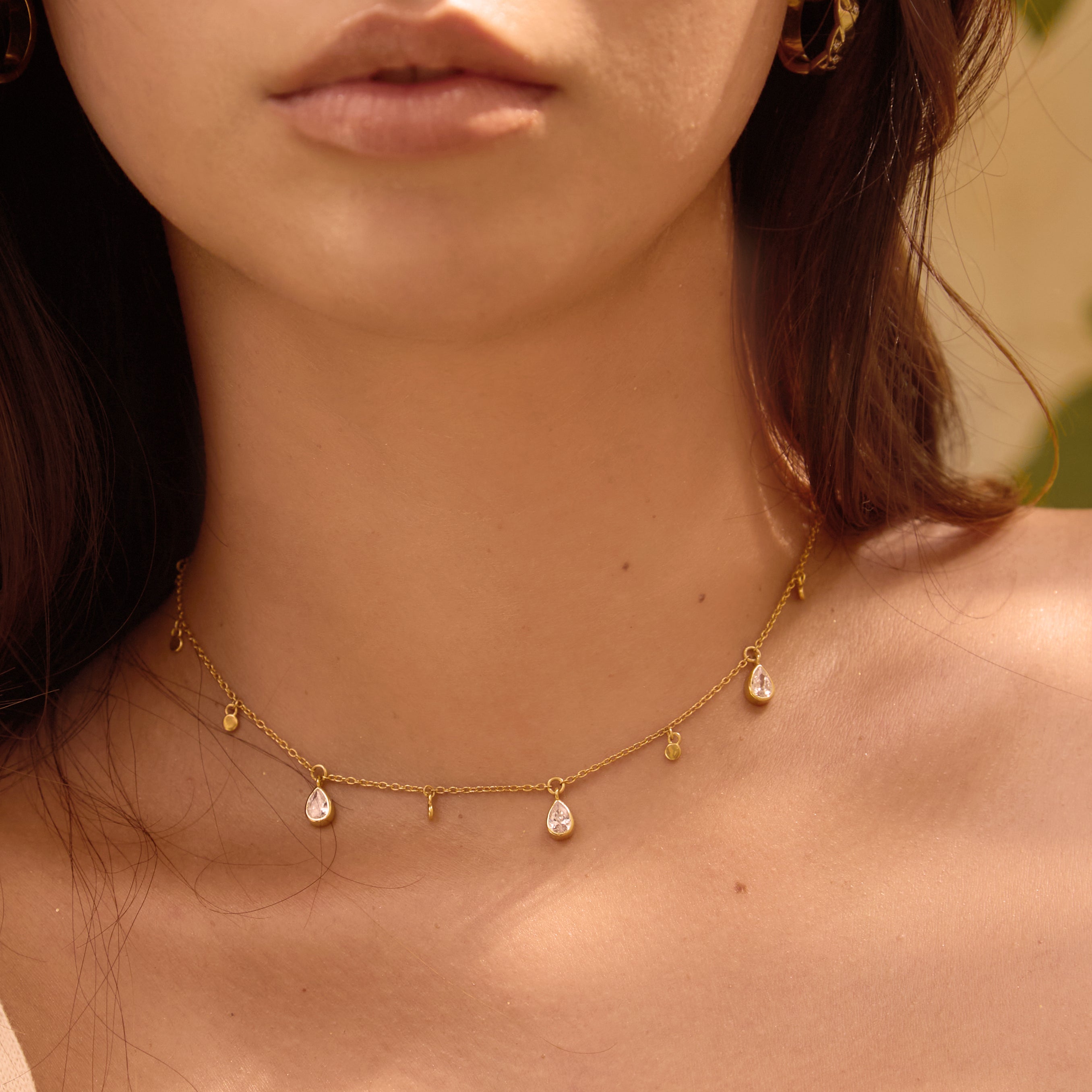 Close-up of a woman wearing a delicate gold necklace with small clear stone pendants.