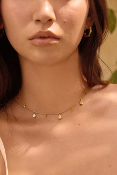 Close-up of a woman wearing a delicate gold necklace with small clear stone pendants.