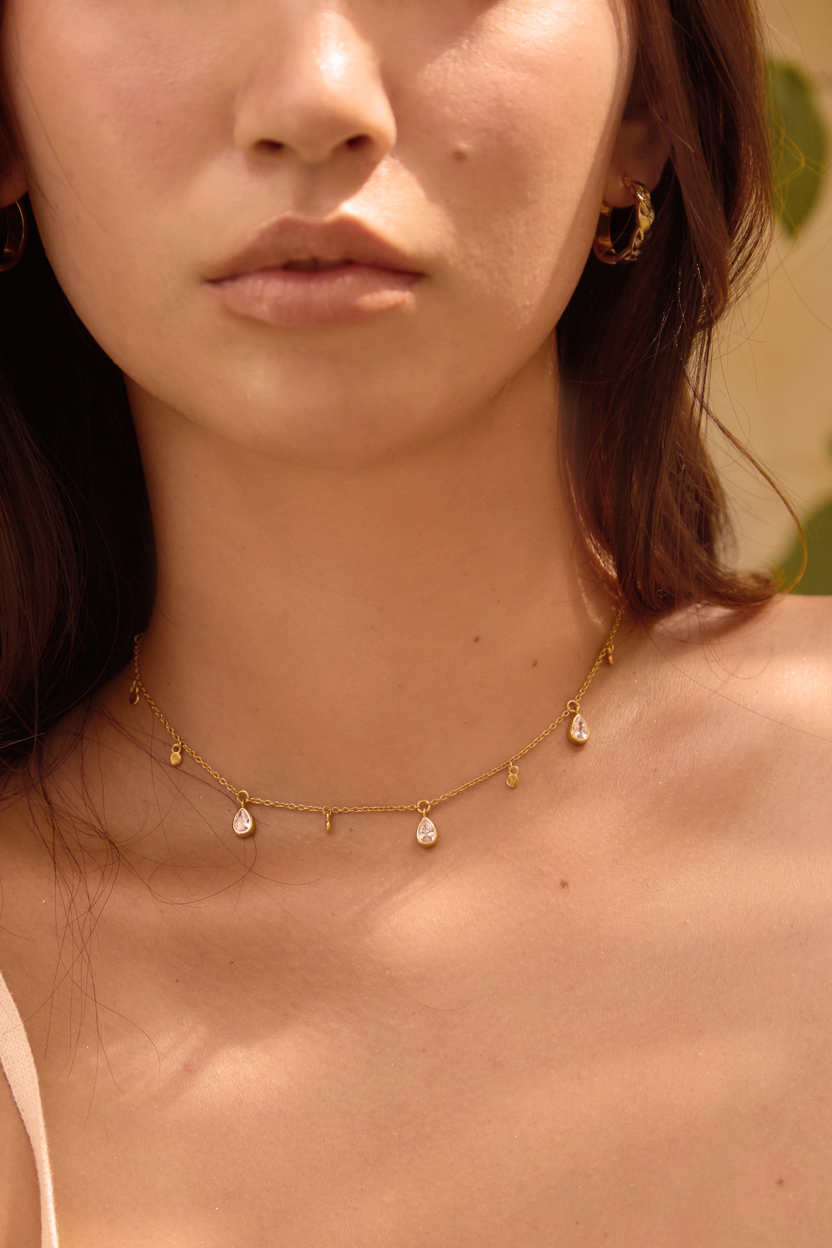 Close-up of a woman wearing a delicate gold necklace with small clear stone pendants.