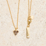 Gold necklace with triangle smoky quartz pendant and bar pendant on a beige background