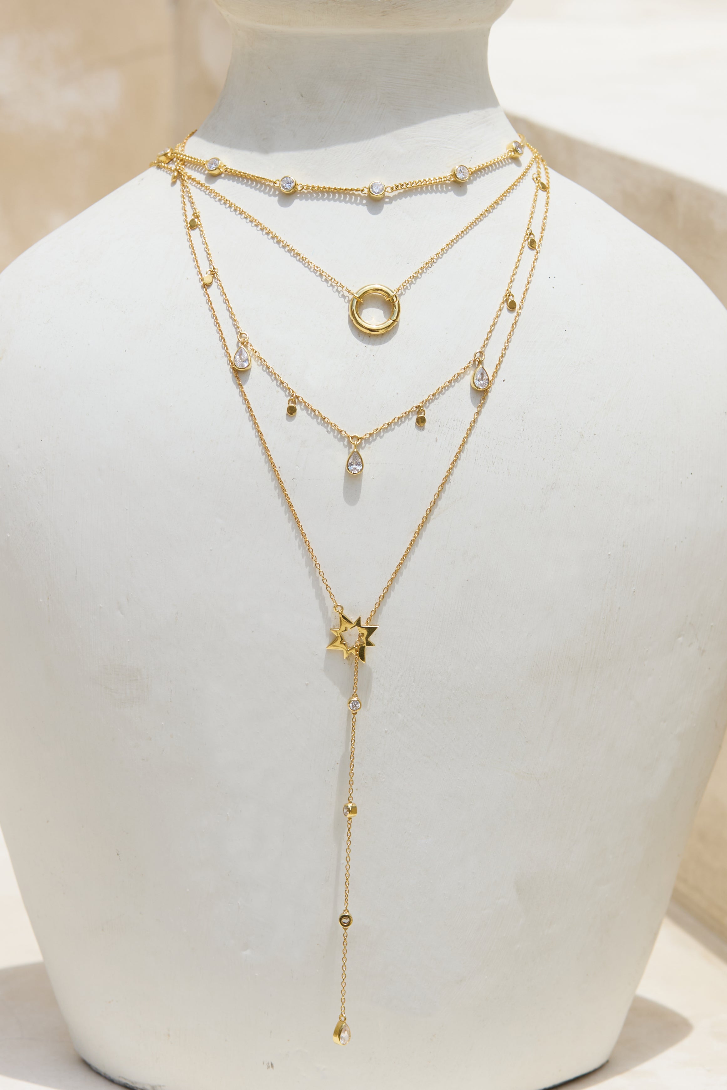 Layered gold necklaces on a white ceramic vase with a plain background