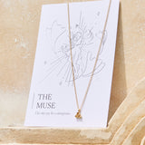 Gold necklace with a yellow citrine triangle pendant on a 'The Muse' affirmation card on a beige background