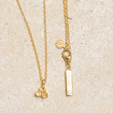 Gold necklace with yellow citrine triangle pendant on a beige background