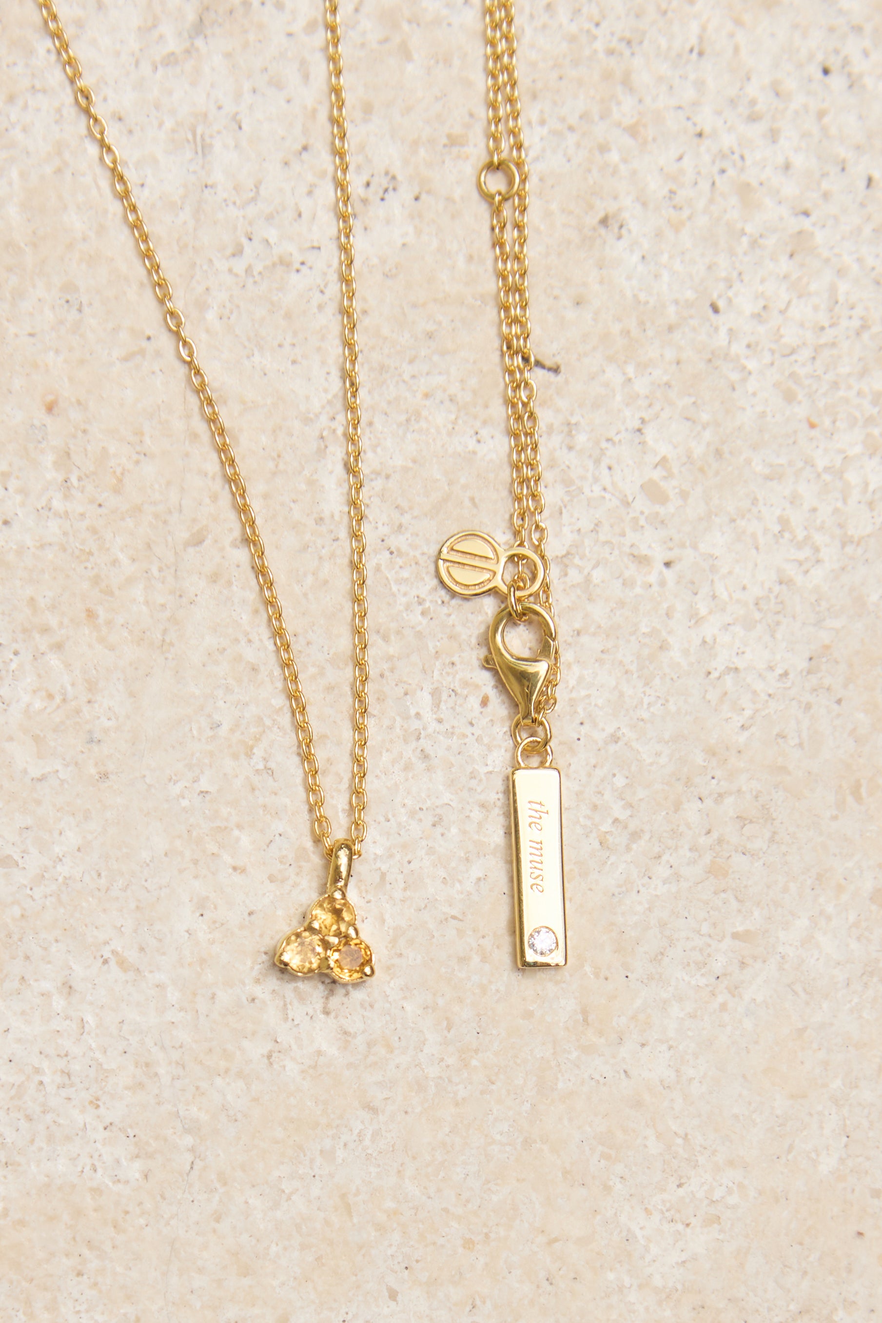 Gold necklace with yellow citrine triangle pendant on a beige background