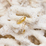 Gold hoop earrings with small clear stones on a textured beige surface