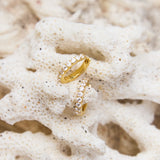 Gold hoop earrings with small clear stones on a textured beige surface