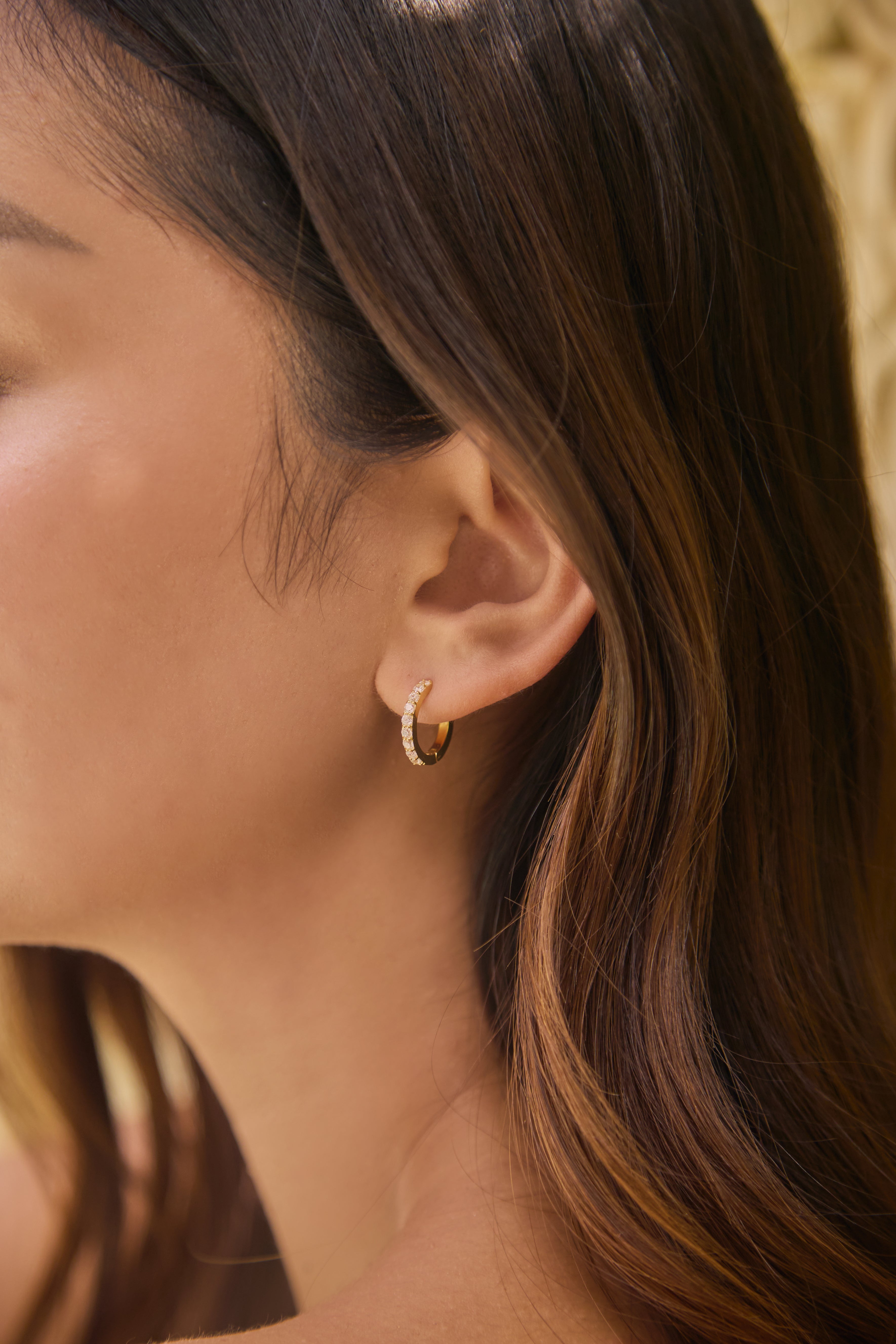Close-up of a person wearing a gold and clear stone hoop earring with soft focus on hair and skin.