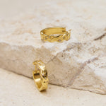 Two gold hoop earrings on a textured stone surface