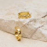 Two gold hoop earrings on a textured stone surface