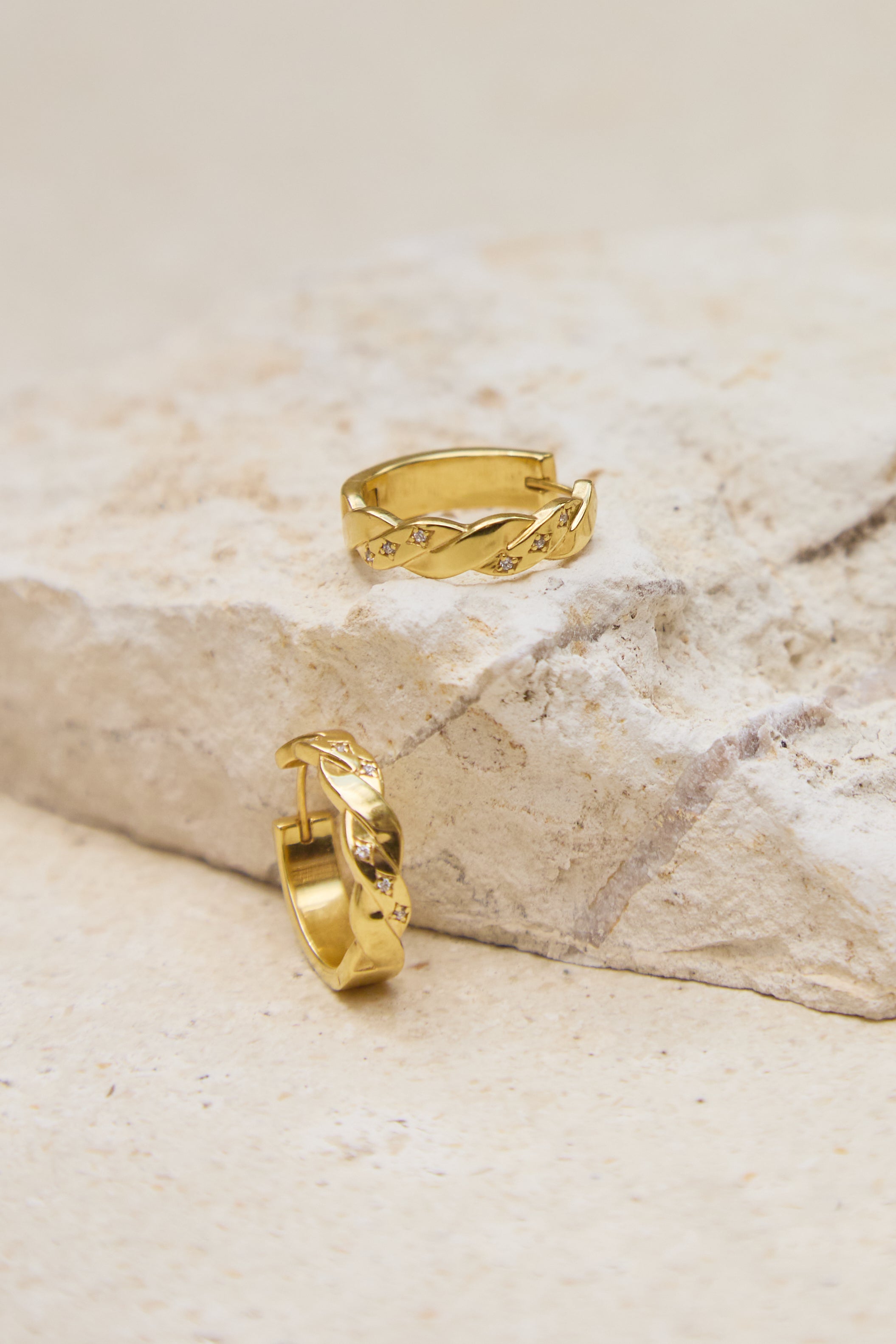 Two gold hoop earrings on a textured stone surface