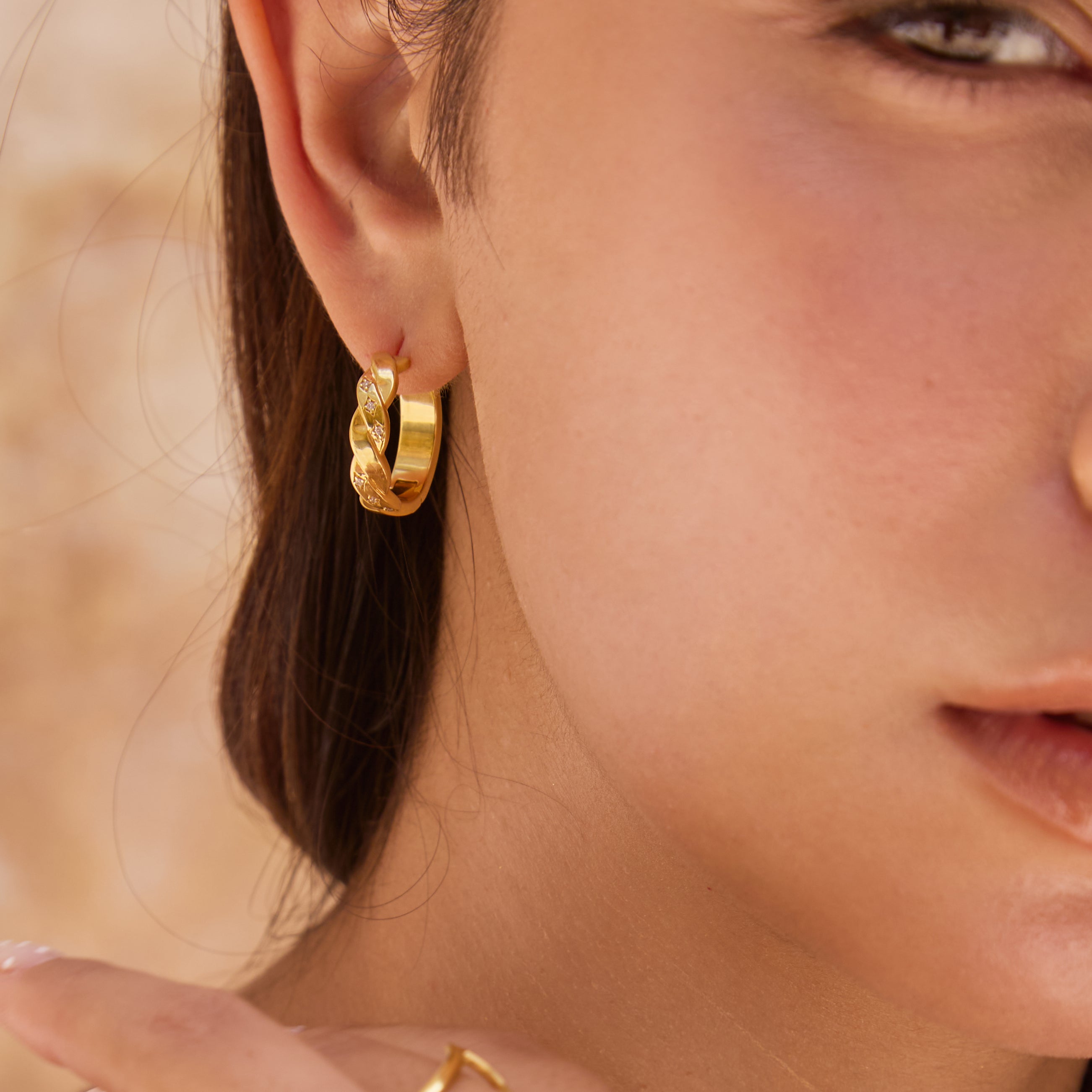 Close-up of a person wearing thick gold hoop earrings and a ring.