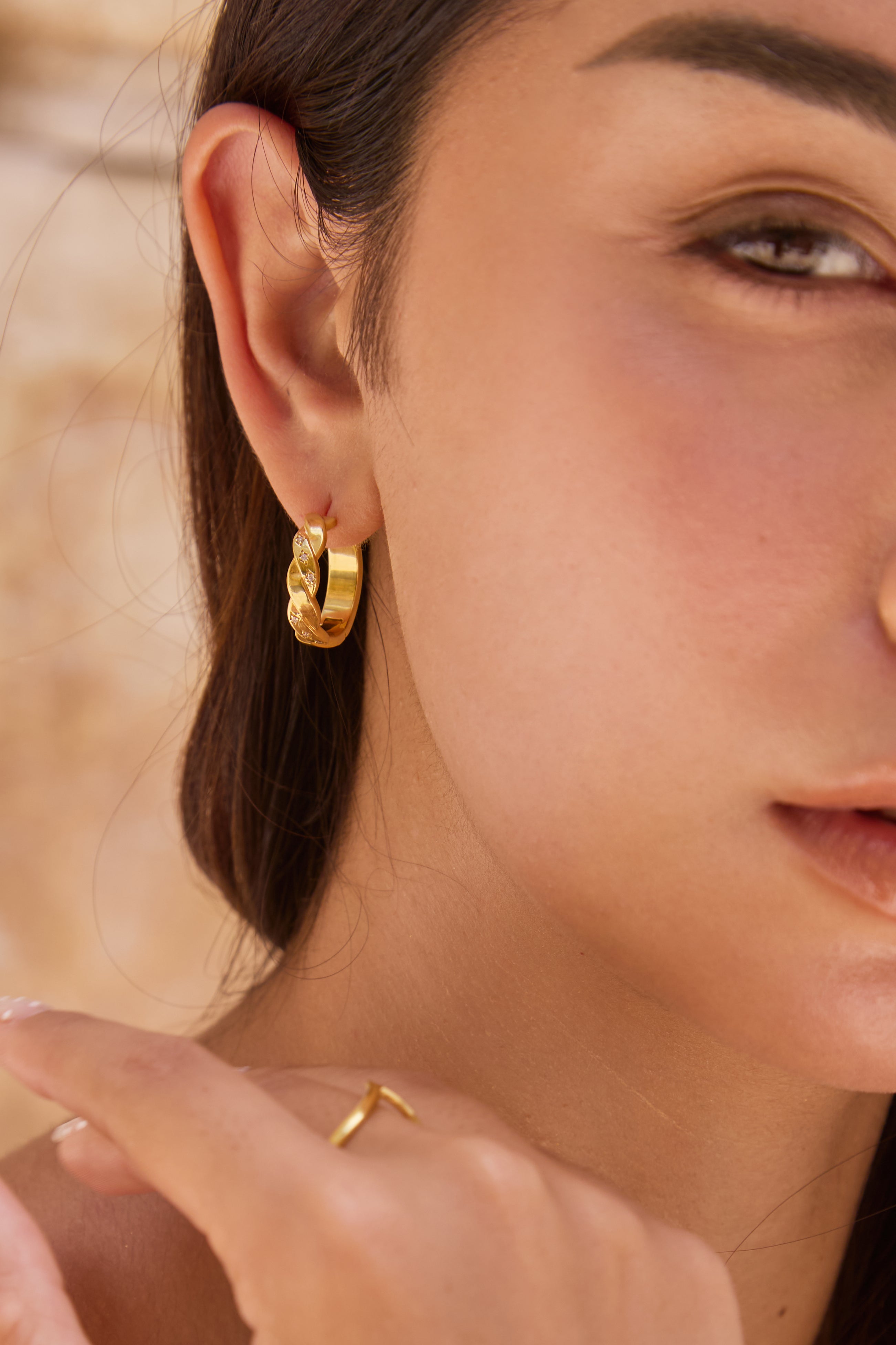 Close-up of a person wearing thick gold hoop earrings and a ring.
