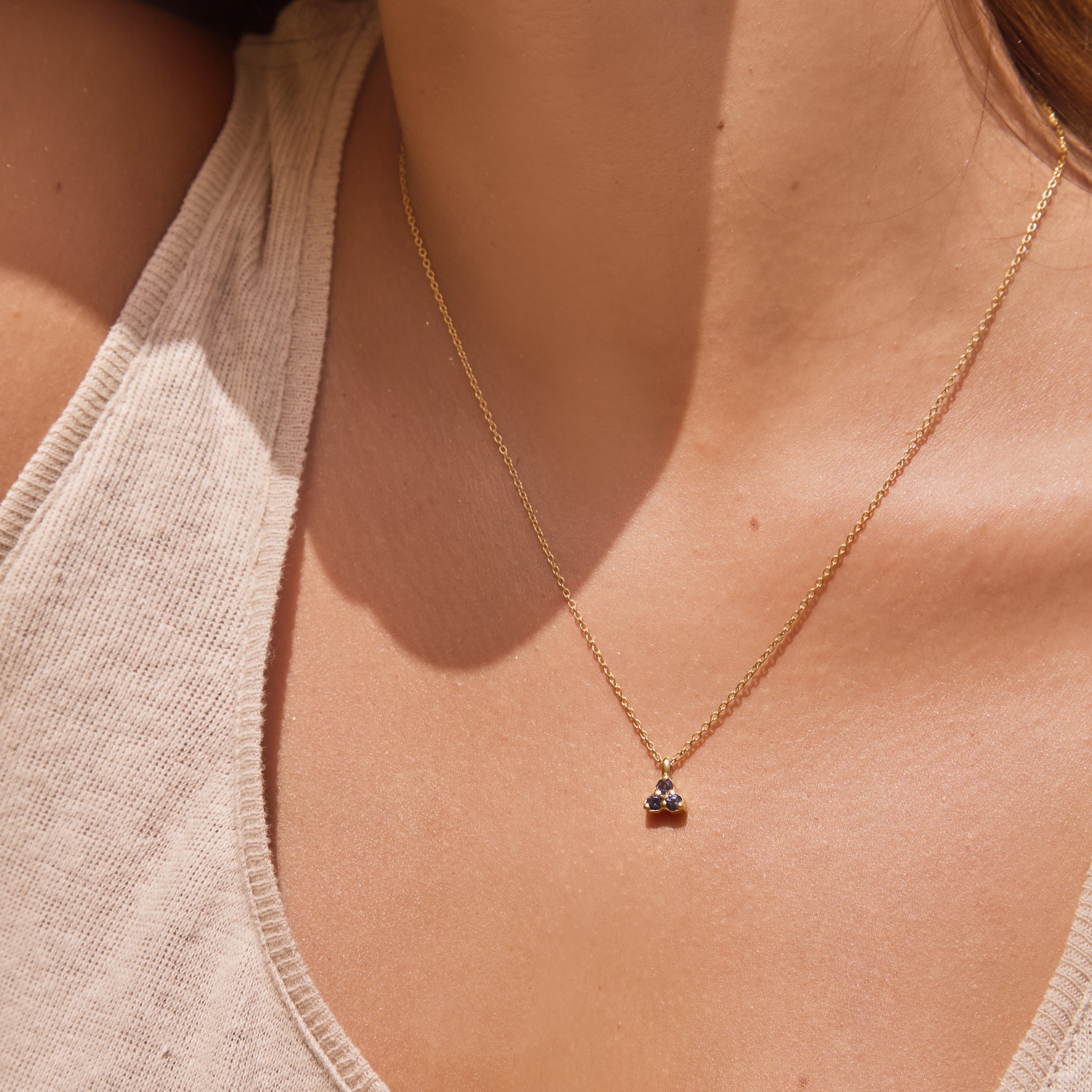 Close-up of a necklace with a small triangle blue iolite pendant on a person wearing a beige tank top.