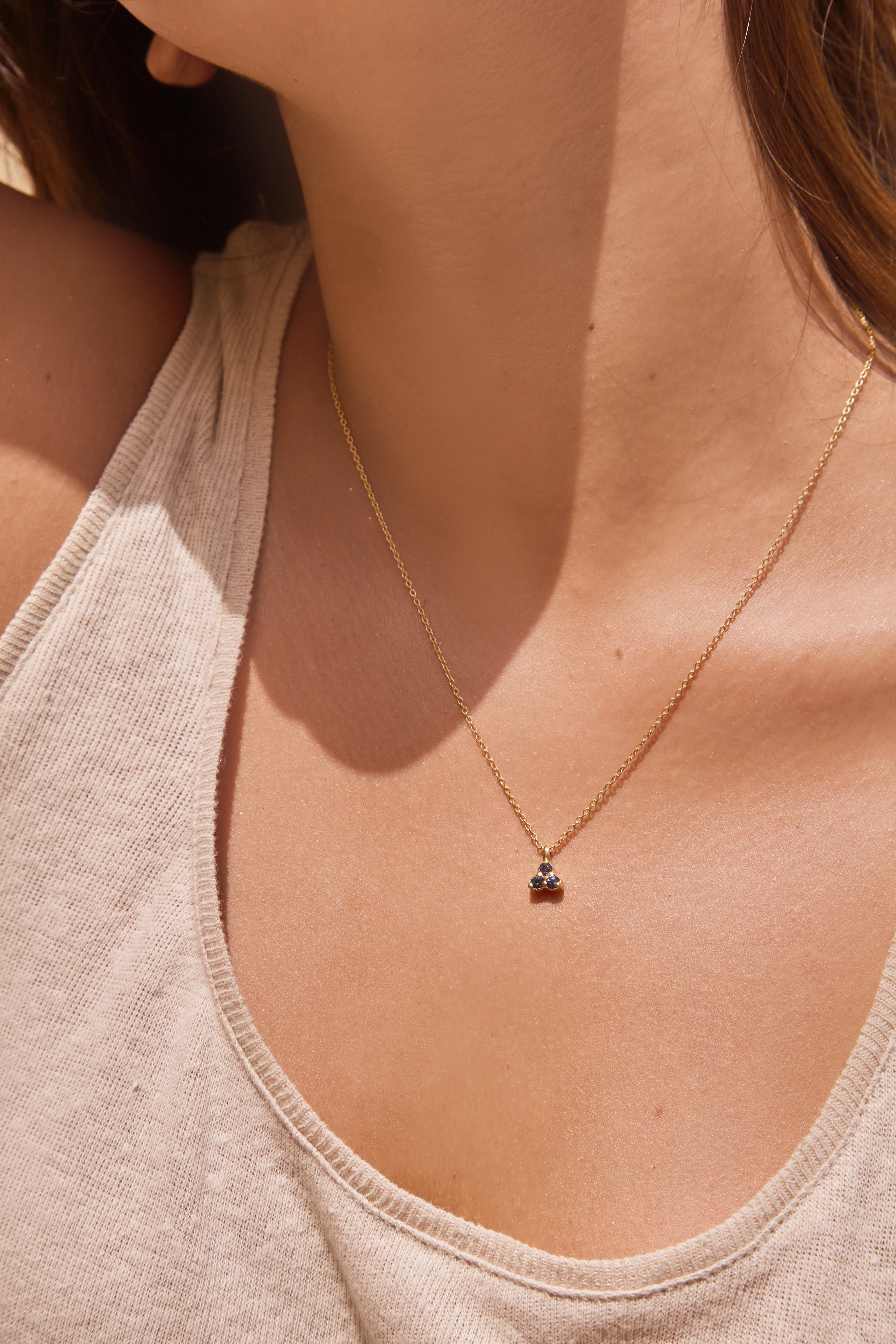 Close-up of a necklace with a small triangle blue iolite pendant on a person wearing a beige tank top.