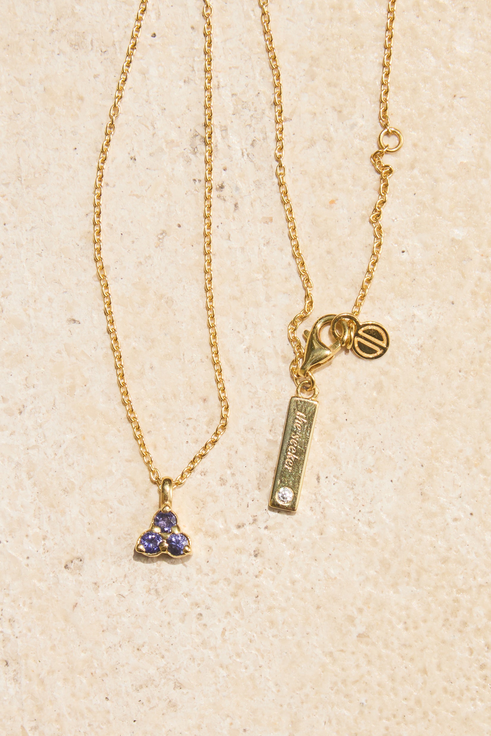 Gold necklace with blue purple iolite triangle pendant on a beige background
