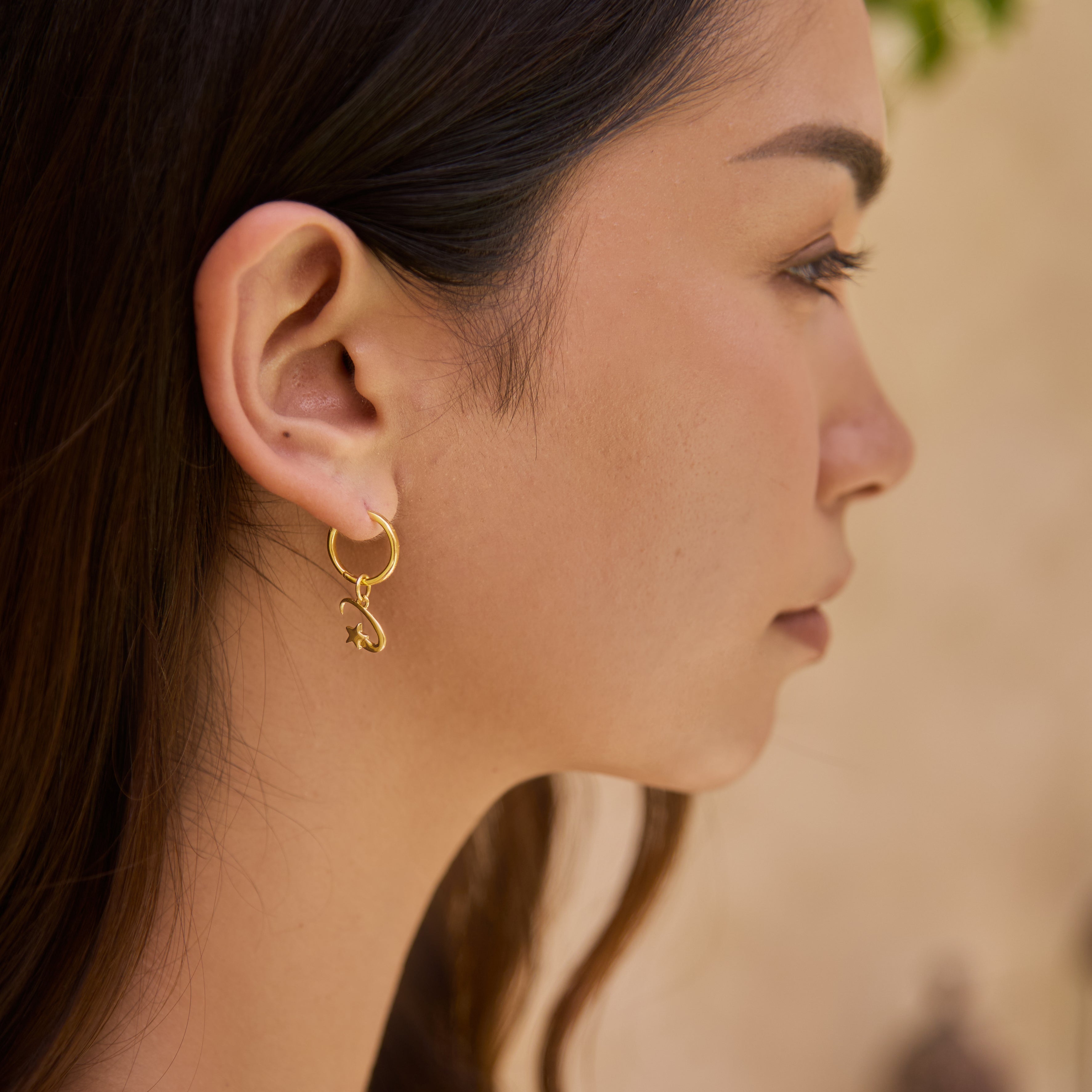 Close-up of a woman wearing a gold earring and shooting star charm with a blurred background