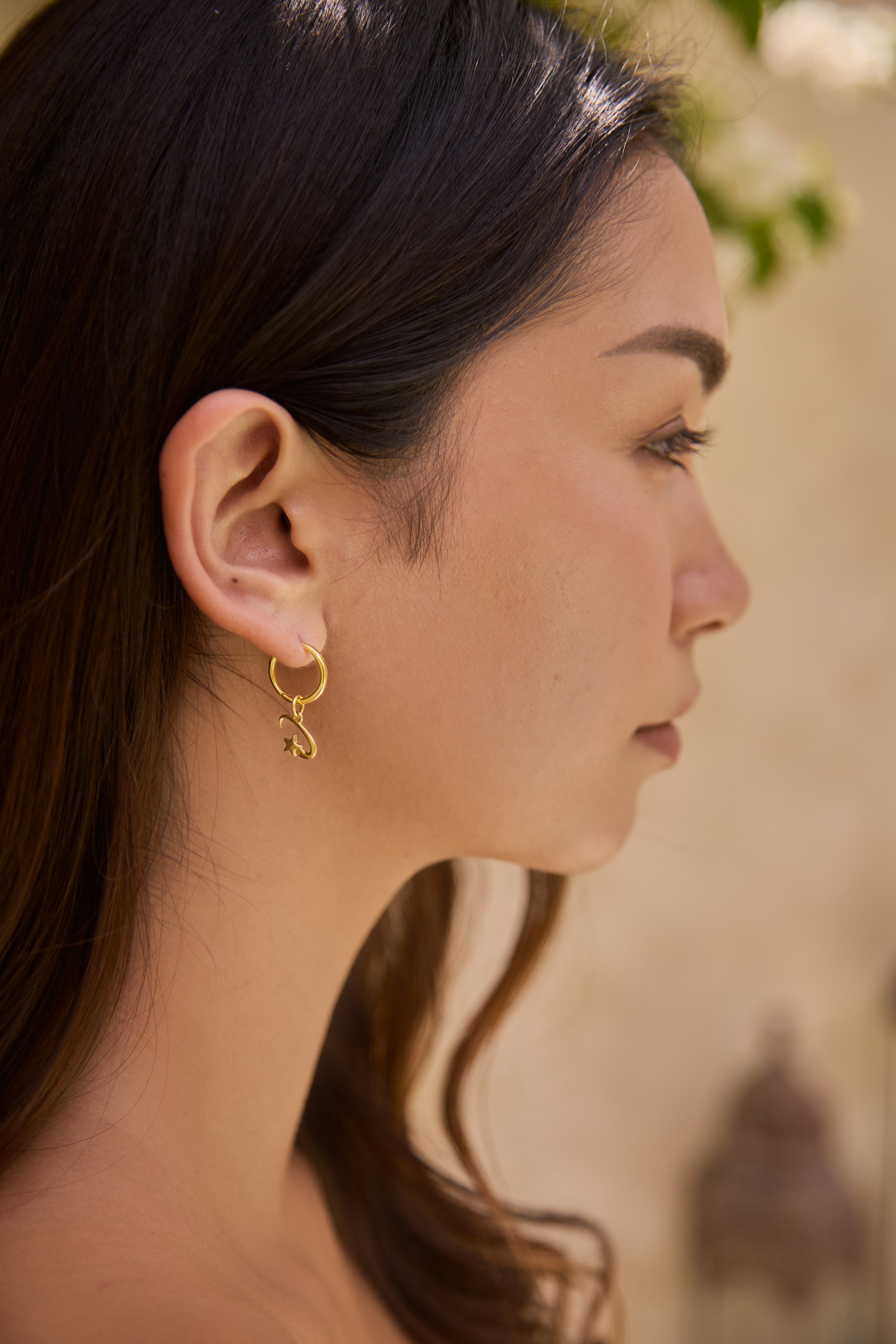 Close-up of a woman wearing a gold earring and shooting star charm with a blurred background