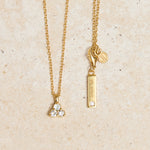 Gold necklace with triangle aquamarine pendant on a beige background