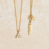 Gold necklace with triangle aquamarine pendant on a beige background