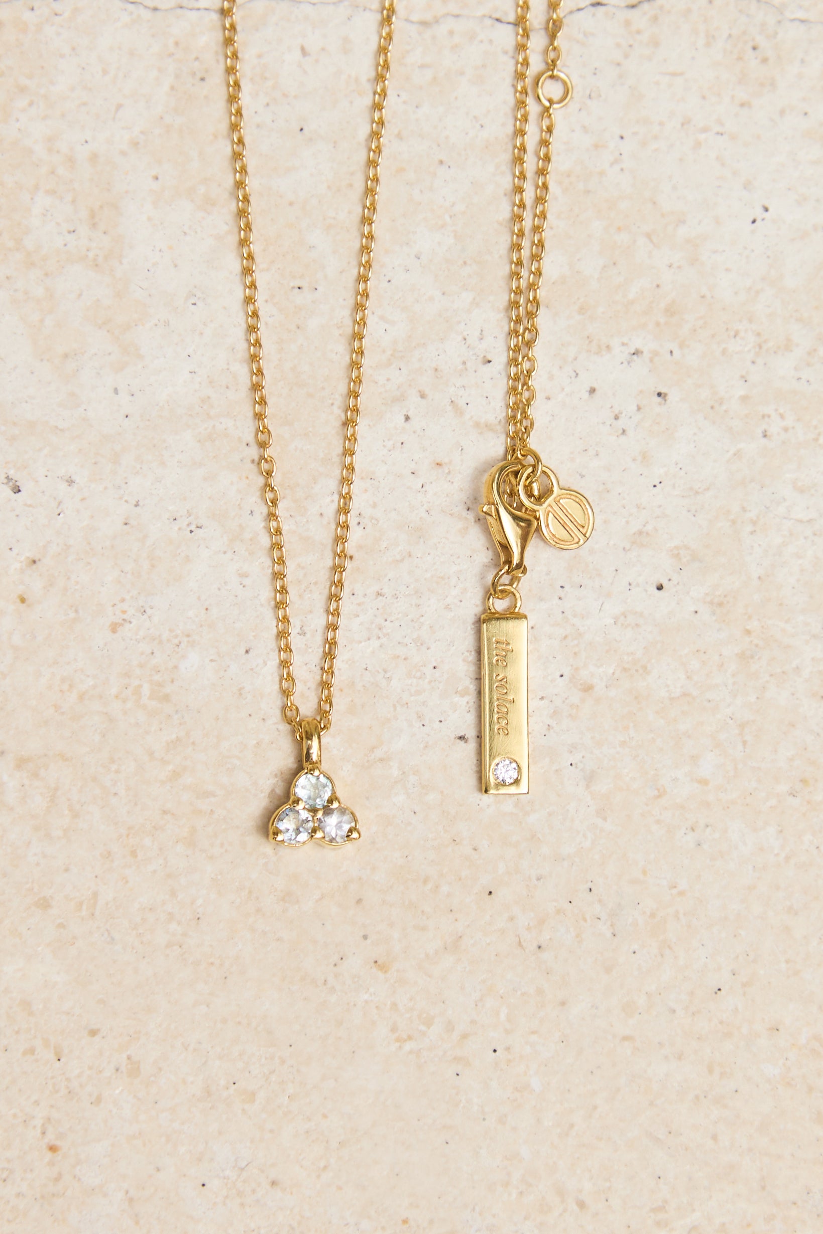 Gold necklace with triangle aquamarine pendant on a beige background