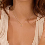 Close-up of a person wearing a delicate gold necklace with a small aquamarine triangle pendant.