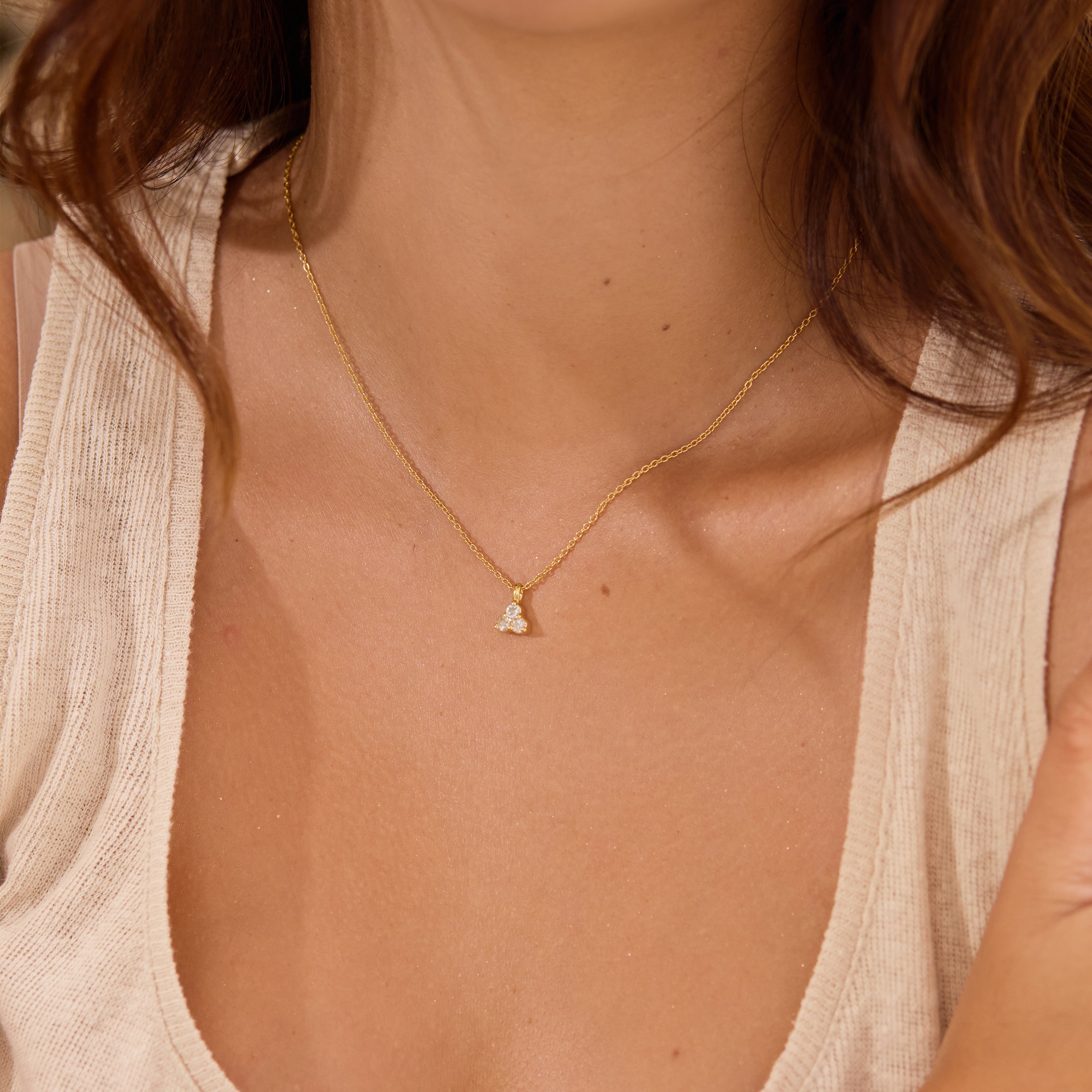 Close-up of a person wearing a delicate gold necklace with a small aquamarine triangle pendant.