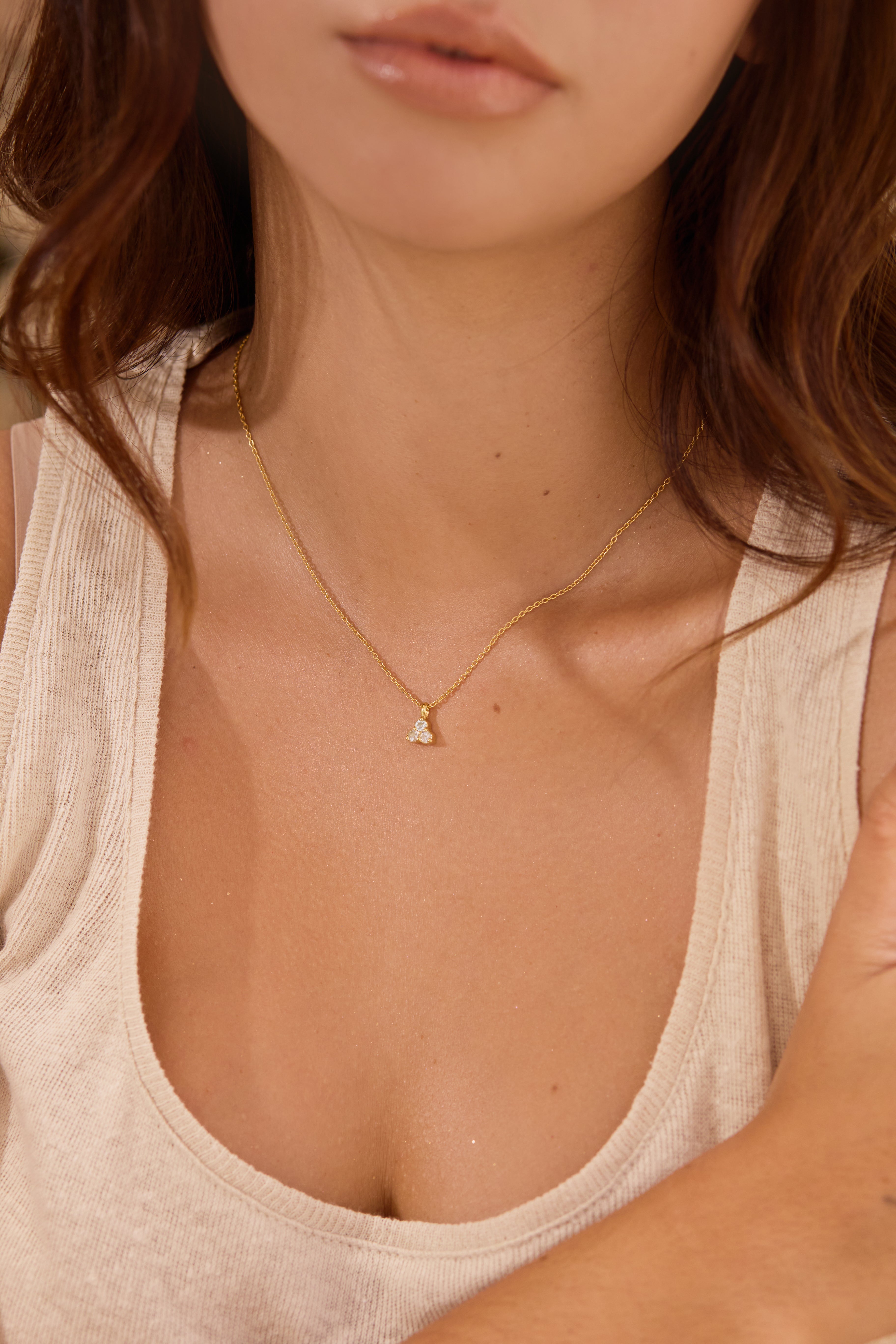 Close-up of a person wearing a delicate gold necklace with a small aquamarine triangle pendant.