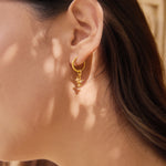 Close-up of a person wearing a gold earring and star sparkle charm with a textured background