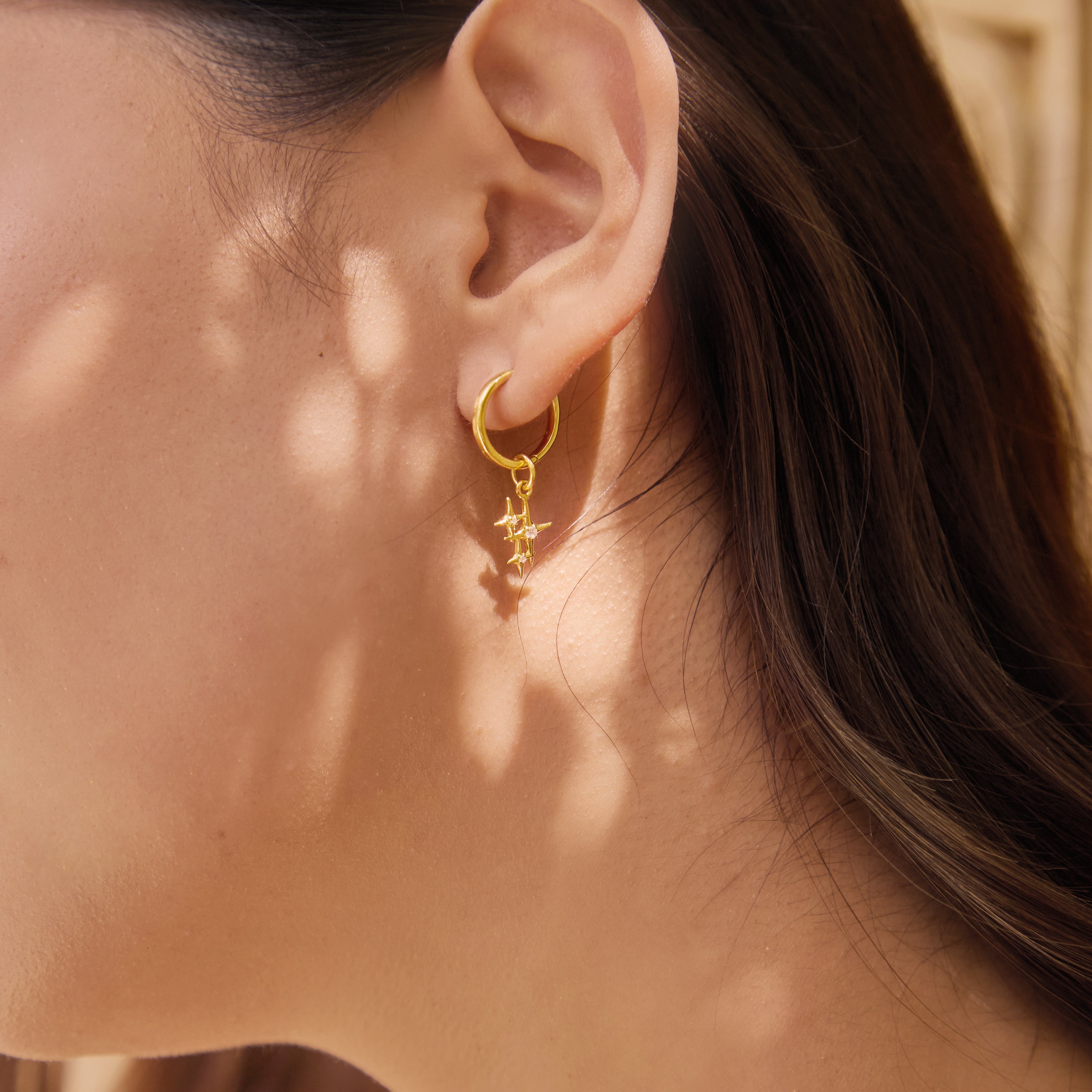 Close-up of a person wearing a gold earring and star sparkle charm with a textured background