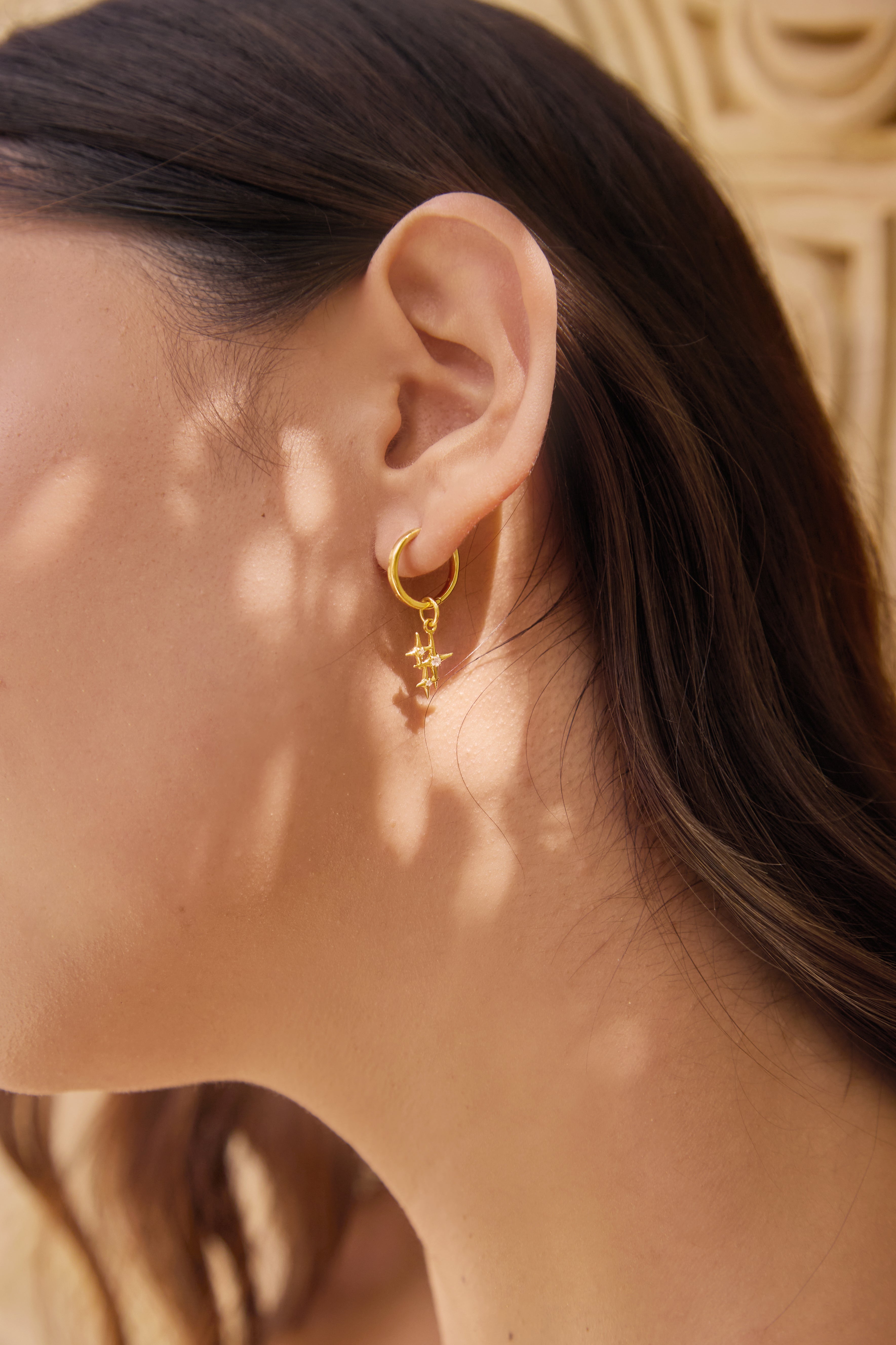 Close-up of a person wearing a gold earring and star sparkle charm with a textured background