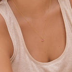 Necklace with a small pink tourmaline triangle pendant worn by a person in a beige tank top.