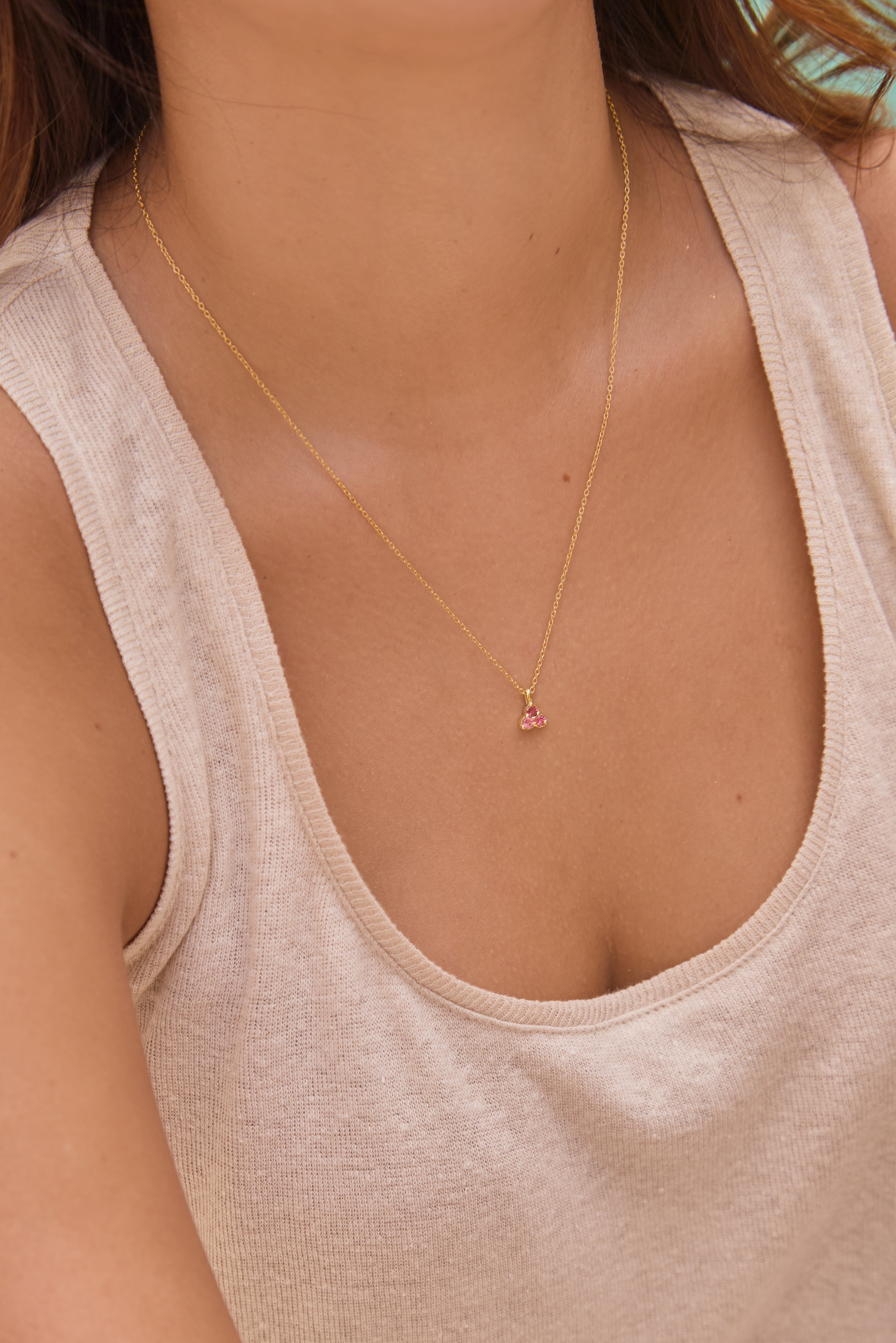 Necklace with a small pink tourmaline triangle pendant worn by a person in a beige tank top.