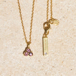 Gold necklace with pink tourmaline triangle-shaped pendant and tag on a beige background