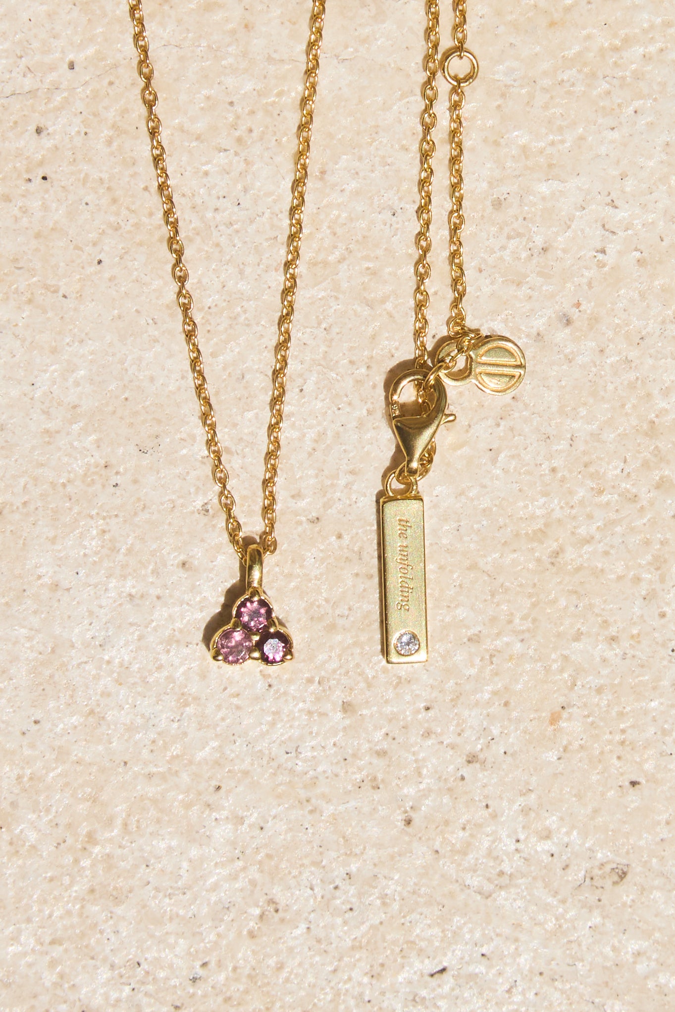 Gold necklace with pink tourmaline triangle-shaped pendant and tag on a beige background