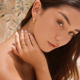 Woman with gold earrings and rings on a neutral background