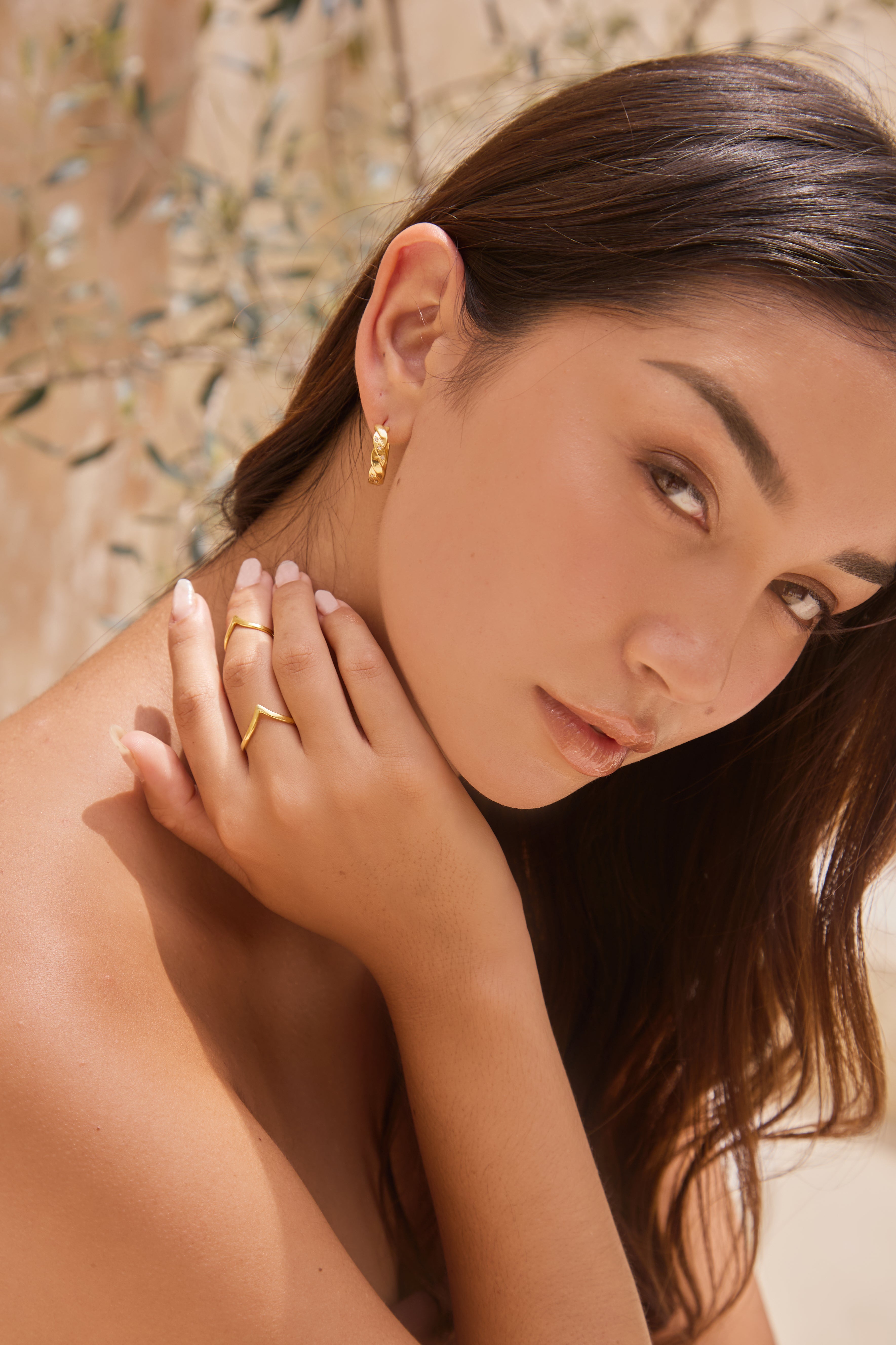 Woman with gold earrings and rings on a neutral background