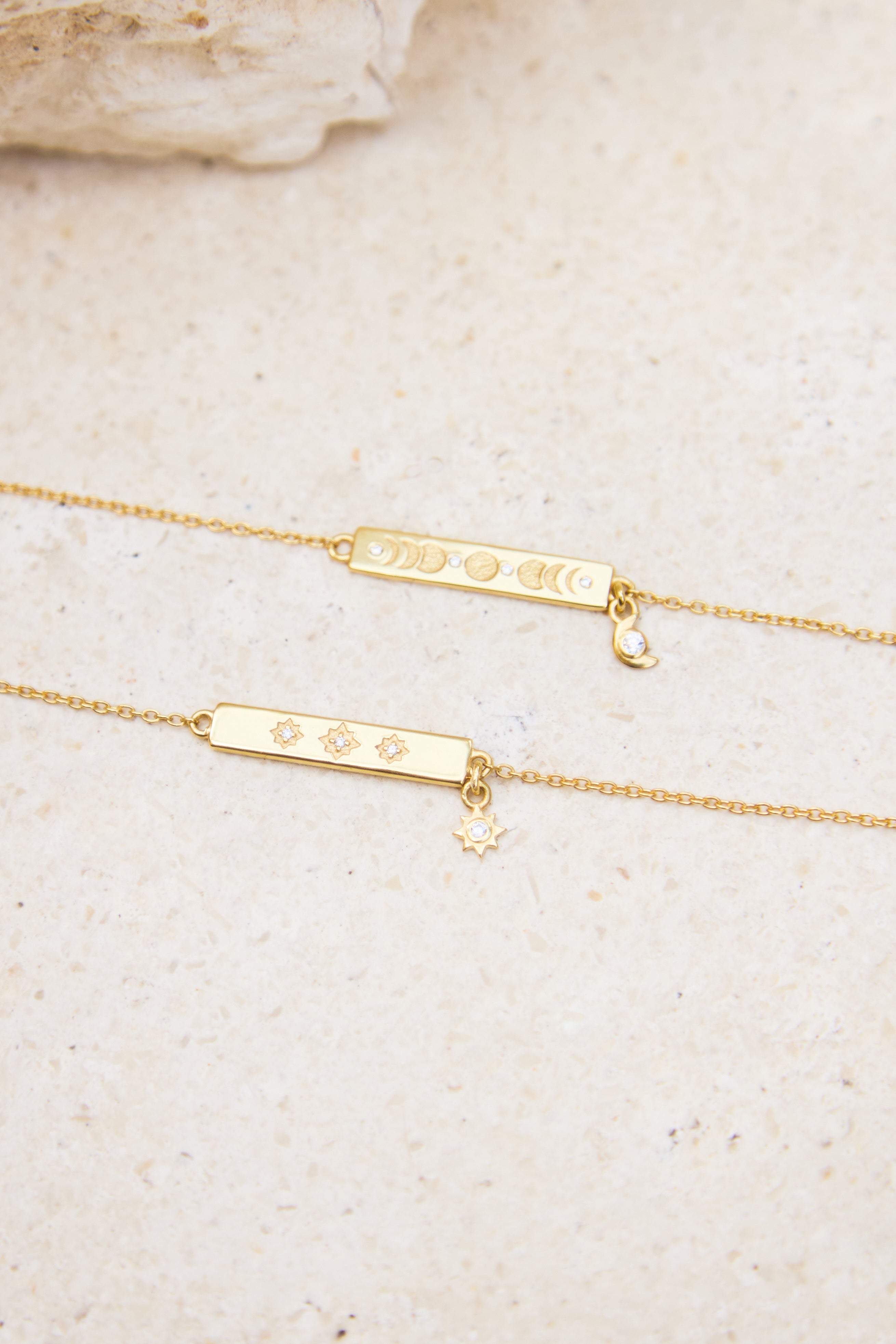 Gold bracelets with engraved designs on a beige stone background